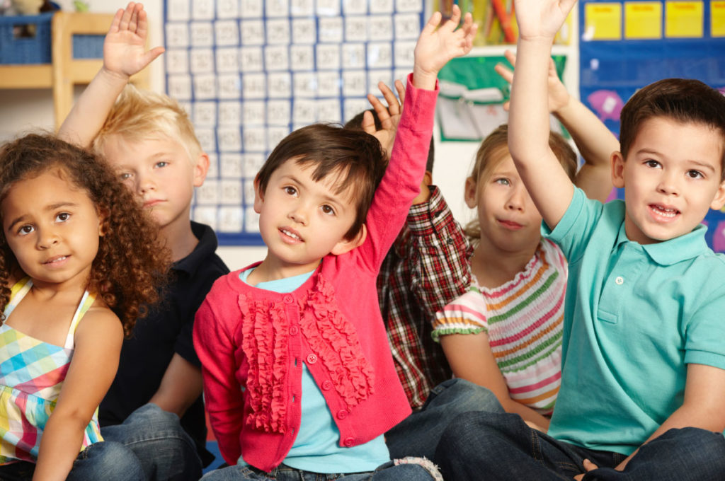 Children in classroom, raising hands